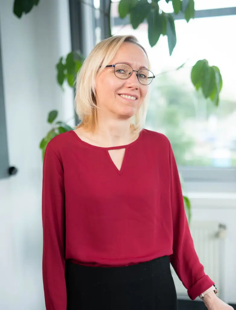 Insa Heller steht am Schreibtisch und lächelt. Sie ist Expertin für digitale Lohnabrechnung und Nettolohnoptimierung.