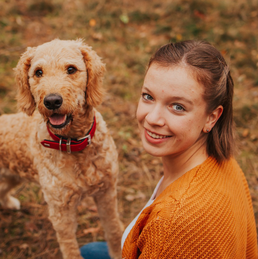 Lena Standke, Inhaberin der Mindful Souls Dogs GmbH, sitzt lächelnd neben einem Hund im Wald